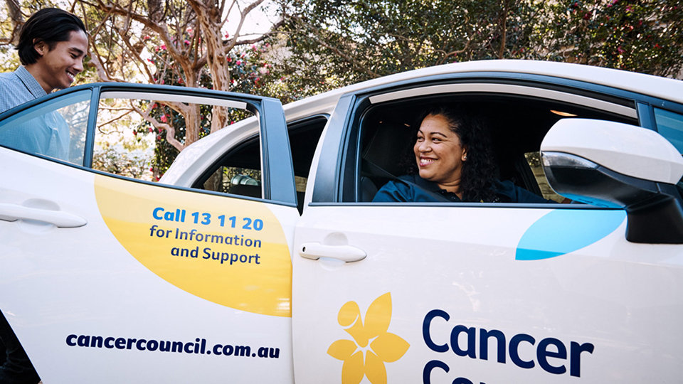 A woman sits in a Cancer Council car, talking to someone outside the vehicle.