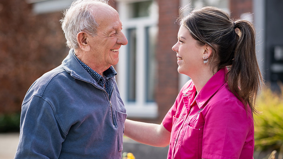 A woman smiles and talks with a man outdoors.