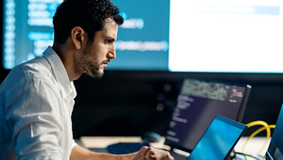 A man is working at a desk with multiple monitors displaying code.