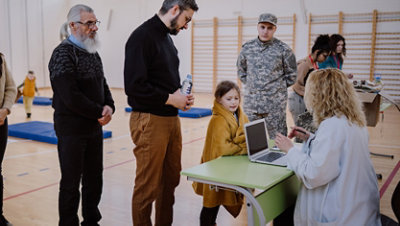 Volunteer talking with a refugee and their child while using the laptop at a refugee shelter.