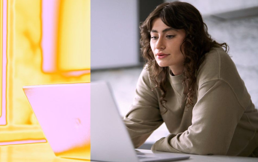 Une personne travaille sur un ordinateur portable, assise à une table, avec un fond lumineux aux tons jaunes et roses.