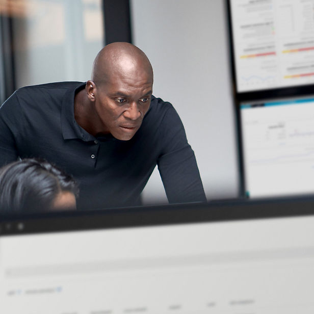 Ein glatzköpfiger schwarzer Mann in einem schwarzen Hemd, der in einem Büro aufmerksam auf einen Computerbildschirm schaut.