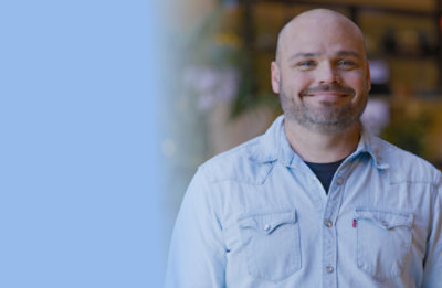 Close-up portrait of a person wearing a light blue denim shirt in an indoor setting.