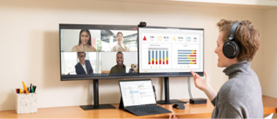 A person wearing headphones participates in a video conference call with four others displayed on a dual monitor setup.