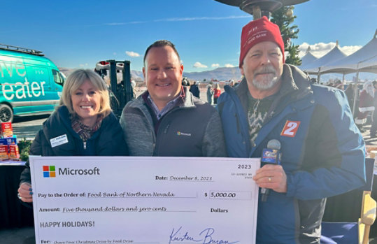 Three people are standing outside holding a large donation check for the Food Bank of Northern Nevada.