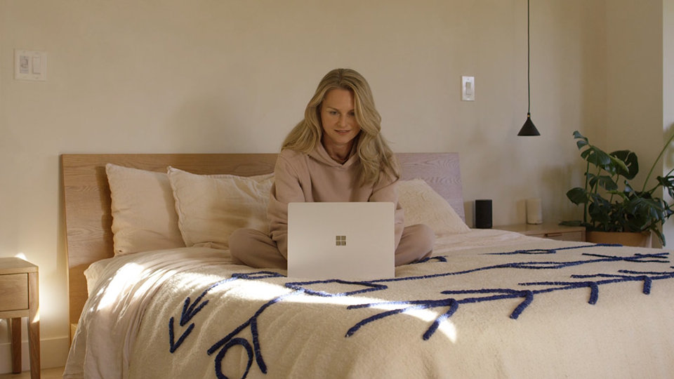 A user sits on the sofa while typing on her Surface Laptop 4.