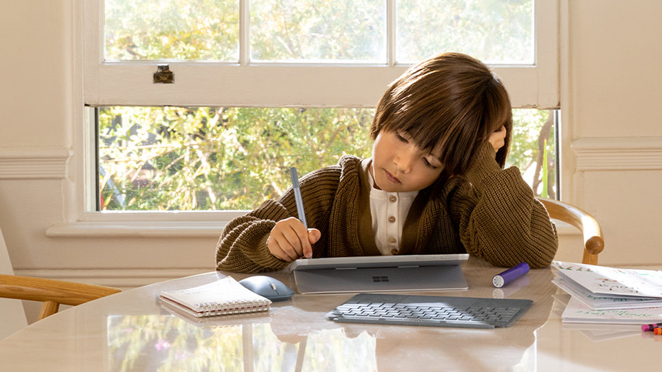 A child uses their Surface Go device at a table.