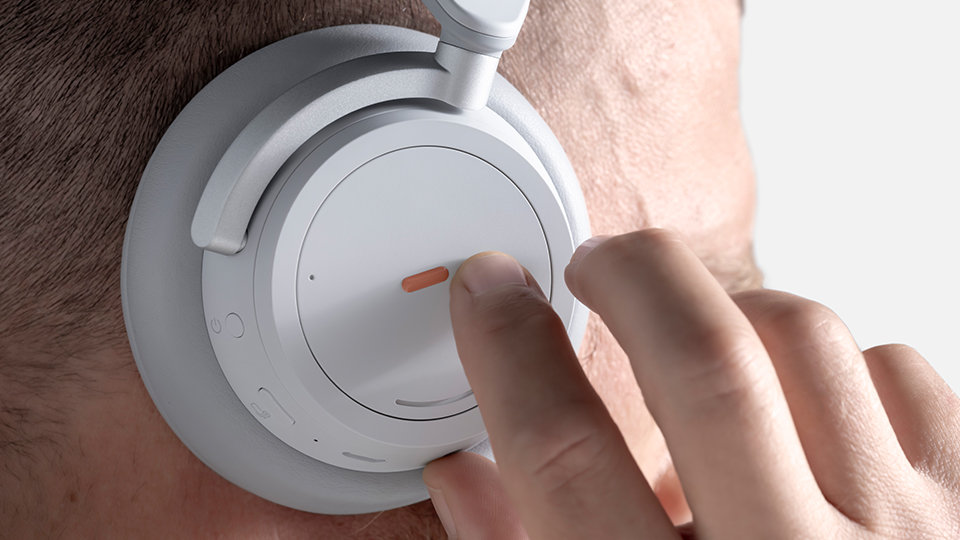 Le mani di una persona che toccano un adesivo di Surface Adaptive Kit sulla cuffia di Surface Headphones.