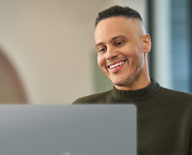 En person, der arbejder på sin bærbare computer og smiler