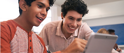 Two young men are smiling while using a tablet.