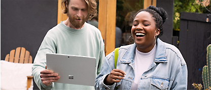 En mand og kvinde, der griner, mens de holder en Microsoft Surface-tablet.