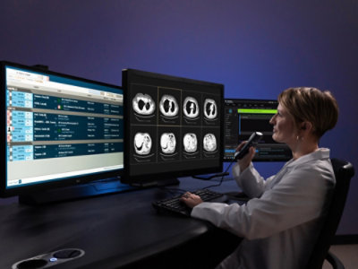 Person reviewing medical scans on multiple monitors at a workstation.
