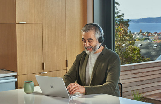 A person on a video call uses a Surface Laptop Go 2 for Business and a Microsoft Modern Wireless Headset for Business.