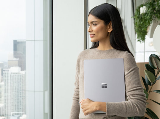 A person holds Surface Laptop 5 for Business in one hand while looking out a window.