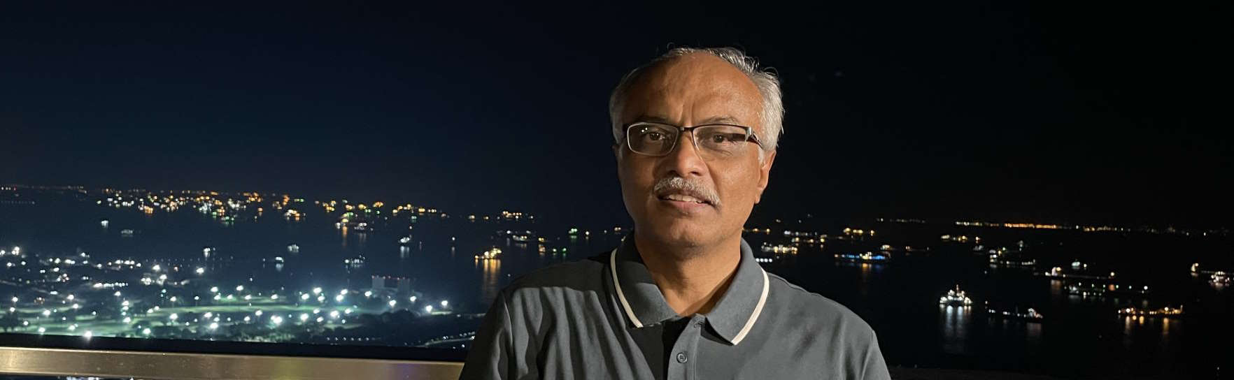 Srikantan Sankaran on a glass balcony overlooking a waterfront at night