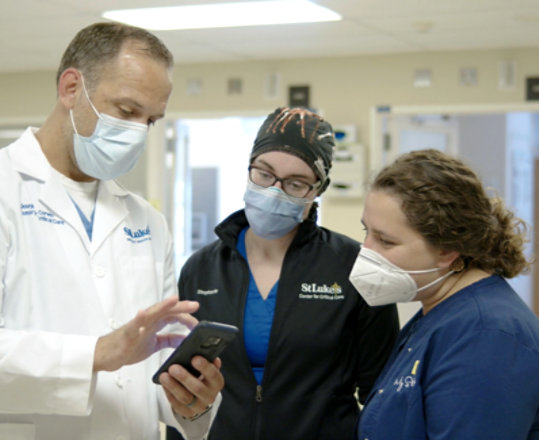 Three medical professionals wearing PPE looking at a mobile device.