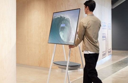 Man rolling a Surface Hub 2S down a hallway on Steelcase Roam Mobile Stand.