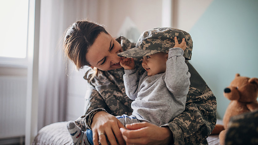 A soldier laughs as she cuddles her baby.