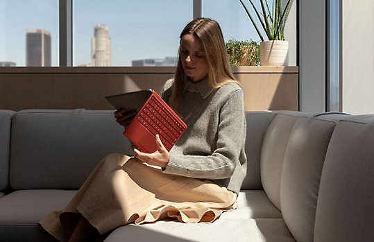 A person seated on a couch using a Surface Pro with red keyboard