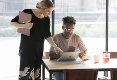 Duas pessoas a trabalharem em conjunto. Uma pessoa está a segurar um Surface Laptop fechado enquanto a outra está a trabalhar num Surface Laptop no modo de estúdio.