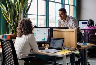 Ảnh hai người trong không gian văn phòng chung đang trò chuyện qua vách ngăn của bàn làm việc