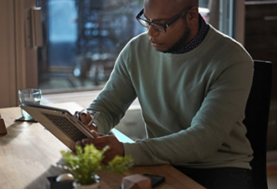 صورة لشخص يجلس في غرفة ذات إضاءة خافته ويستخدم قلماً وجهاز كمبيوتر لوحي.