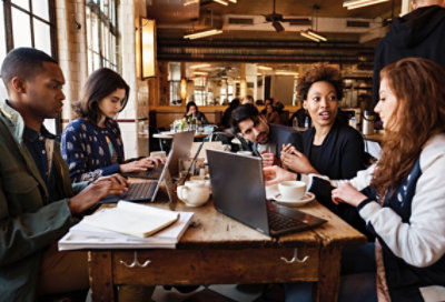 Πέντε άτομα εργάζονται μαζί, σε ένα τραπέζι σε μια καφετέρια. Δύο χρησιμοποιούν φορητούς υπολογιστές και ένα χρησιμοποιεί Surface Pro σε λειτουργία φορητού υπολογιστή