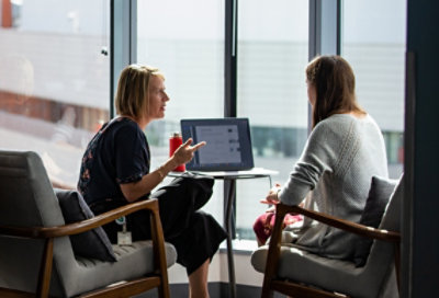 صورة لشخصين يجلسان مقابل بعضهما البعض ويتناقشان ويستخدمان جهاز كمبيوتر محمول على طاولة بينهما.