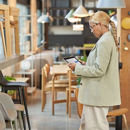 A furniture store employee standing in front of a display of wooden chairs using a tablet