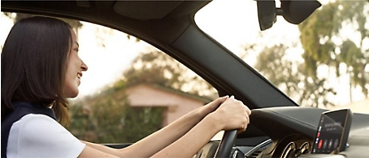 Een vrouw die in een auto rijdt met haar handen op het stuur.