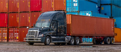 A semi truck is parked in front of containers.
