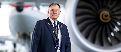 A man in a suit standing in front of an airplane engine.