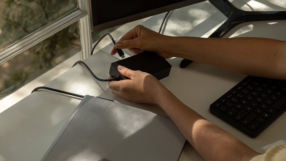 Una persona collega Surface Dock 2 per le aziende a un dispositivo Surface.