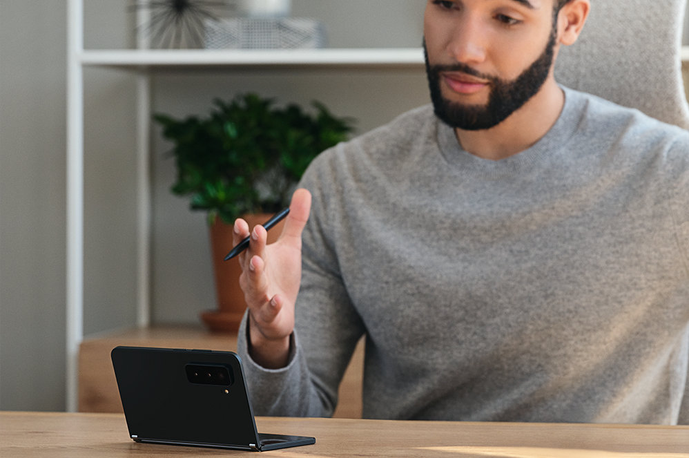 Een persoon zit aan een tafel met een Surface Duo 2 erop.