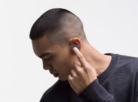 A man adjusts the volume on his Surface Earbuds in Graphite.