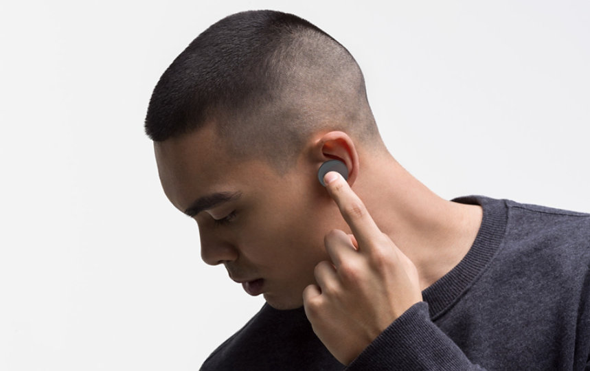 Ein Mann stellt die Lautstärke seiner Surface Earbuds in der Farbe Graphit ein.