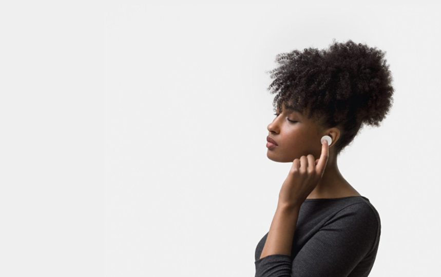 A woman touches Surface Earbuds in her left ear.