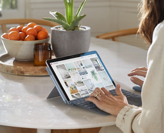 Mężczyzna siedzący w kawiarni razem z kobietą dotykającą ekranu komputera Surface Go 2