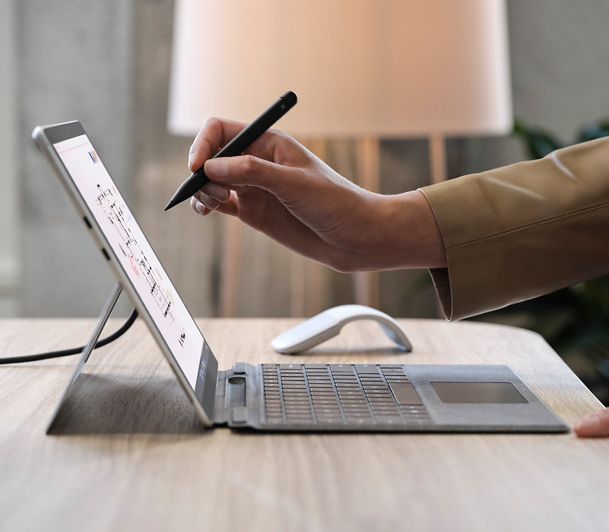  person’s hand holding Surface Slim Pen 2 for Business in front of a Surface device screen.