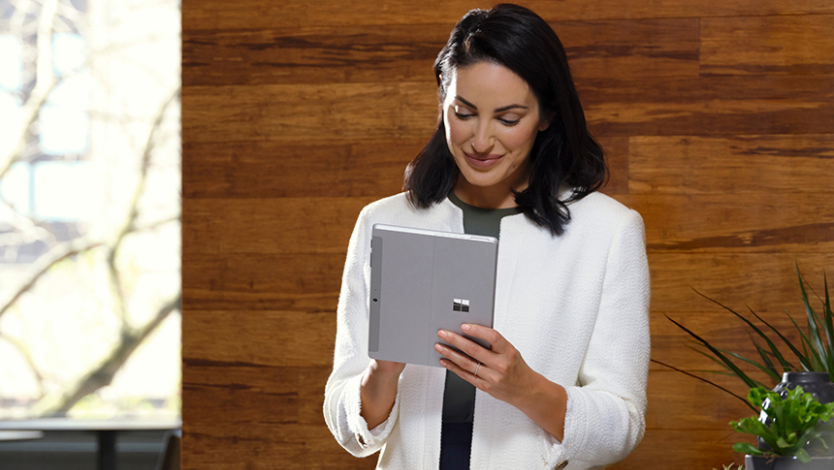 Una mujer parada escribe en un dispositivo Surface Go 4 en modo tableta