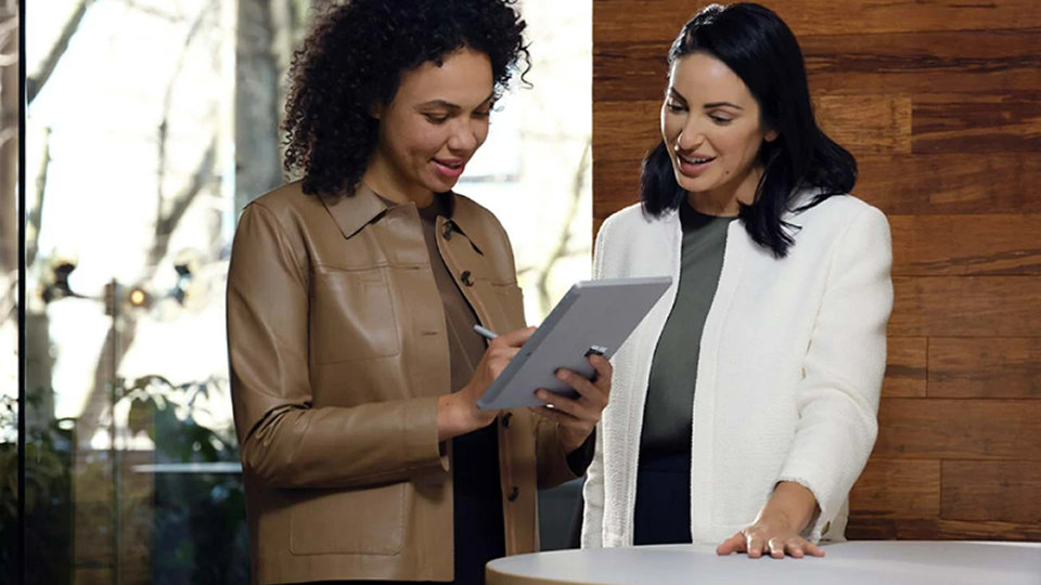 Two co-workers on-the-go at a meeting use Surface Pen to navigate Surface Go 4