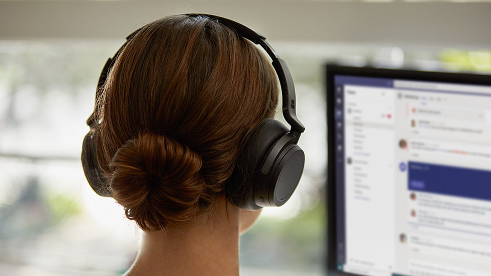 Une personne porte son casque Surface Headphones 2 à un bureau.