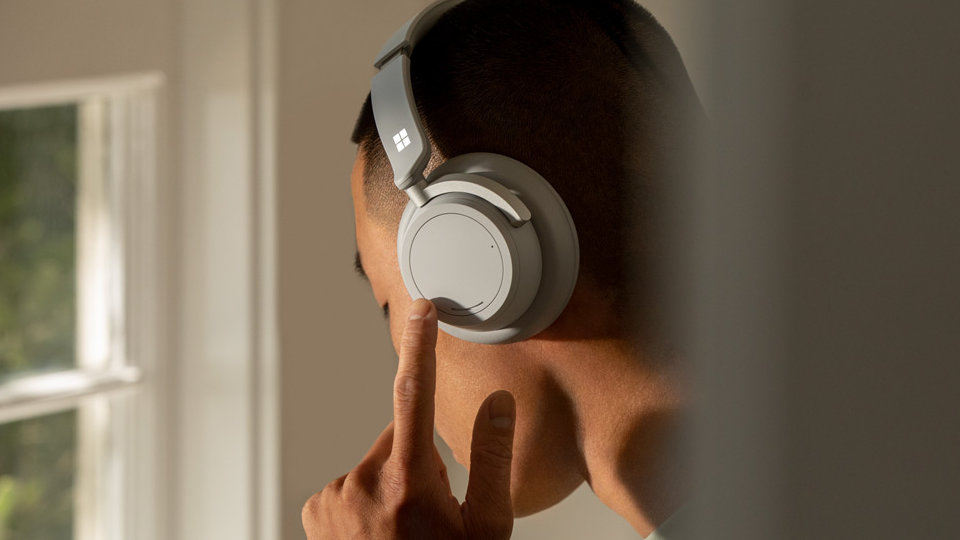 رجل يستخدم قرص الاتصال الأيسر الموجود على الأذن لضبط إلغاء الضوضاء في Surface Headphones 2