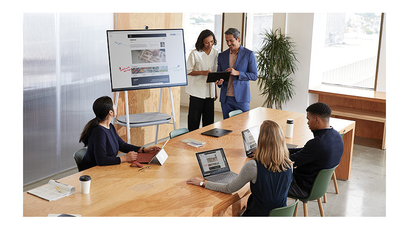 A woman draws on Surface Hub in an office meeting with several people around a table.