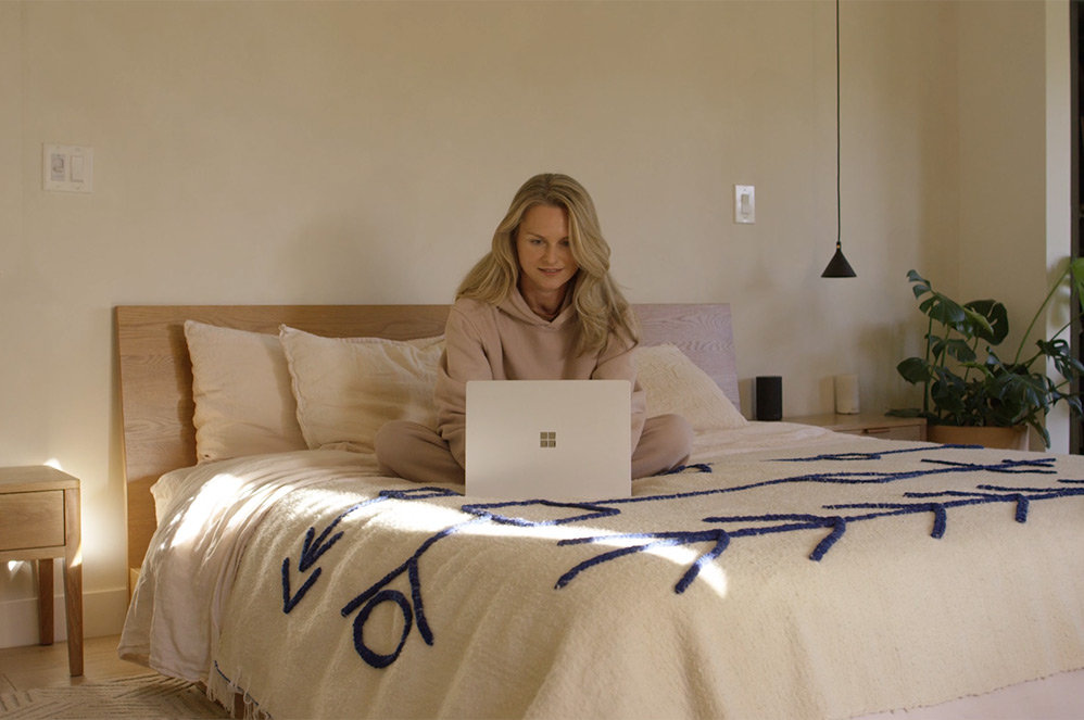 A user sits on the sofa while typing on her Surface Laptop 4