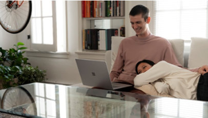 Two people relax on a couch while using the Surface Laptop 3.