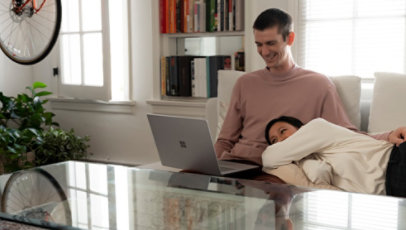 Two people relax on a couch while using the Surface Laptop 3.