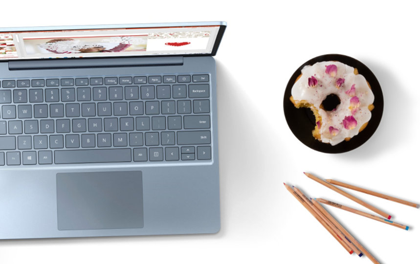 Ein Surface Laptop Gehen Sie von oben auf einen Tisch neben einem Handy, Donut, Bleistiften und Blumenvase.