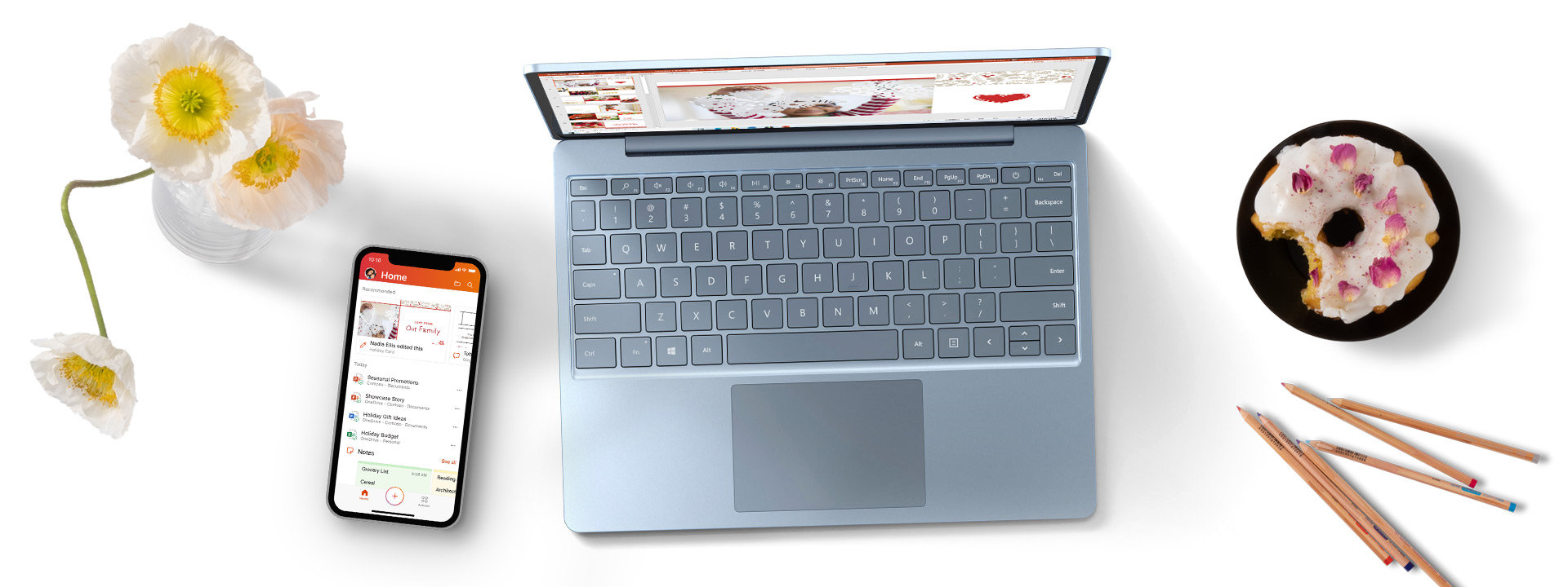 Surface Laptop Go with a phone, pencils, flower vase, and donut on a plate.