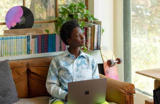 Une femme assise sur son canapé regarde au loin en utilisant son Surface Laptop Go.